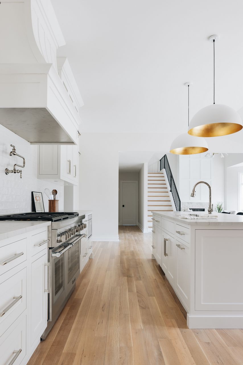 A white island with sink and KOHLER single hole faucet, in a white kitchen with large white range hood and pot filler faucet.