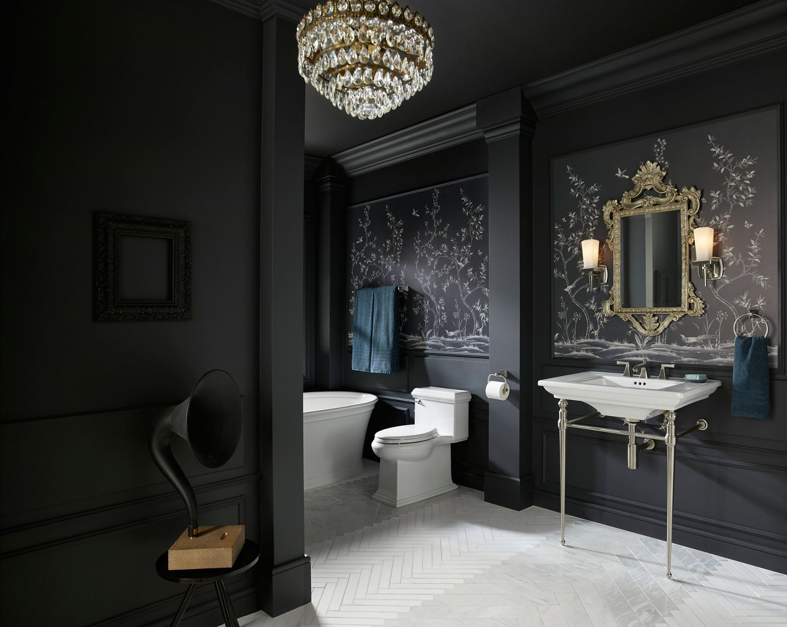 An elegant, moody bathroom with black walls, and white KOHLER Memoirs oval freestanding bath, white Memoirs Classic toilet, and white Memoirs Stately console sink.