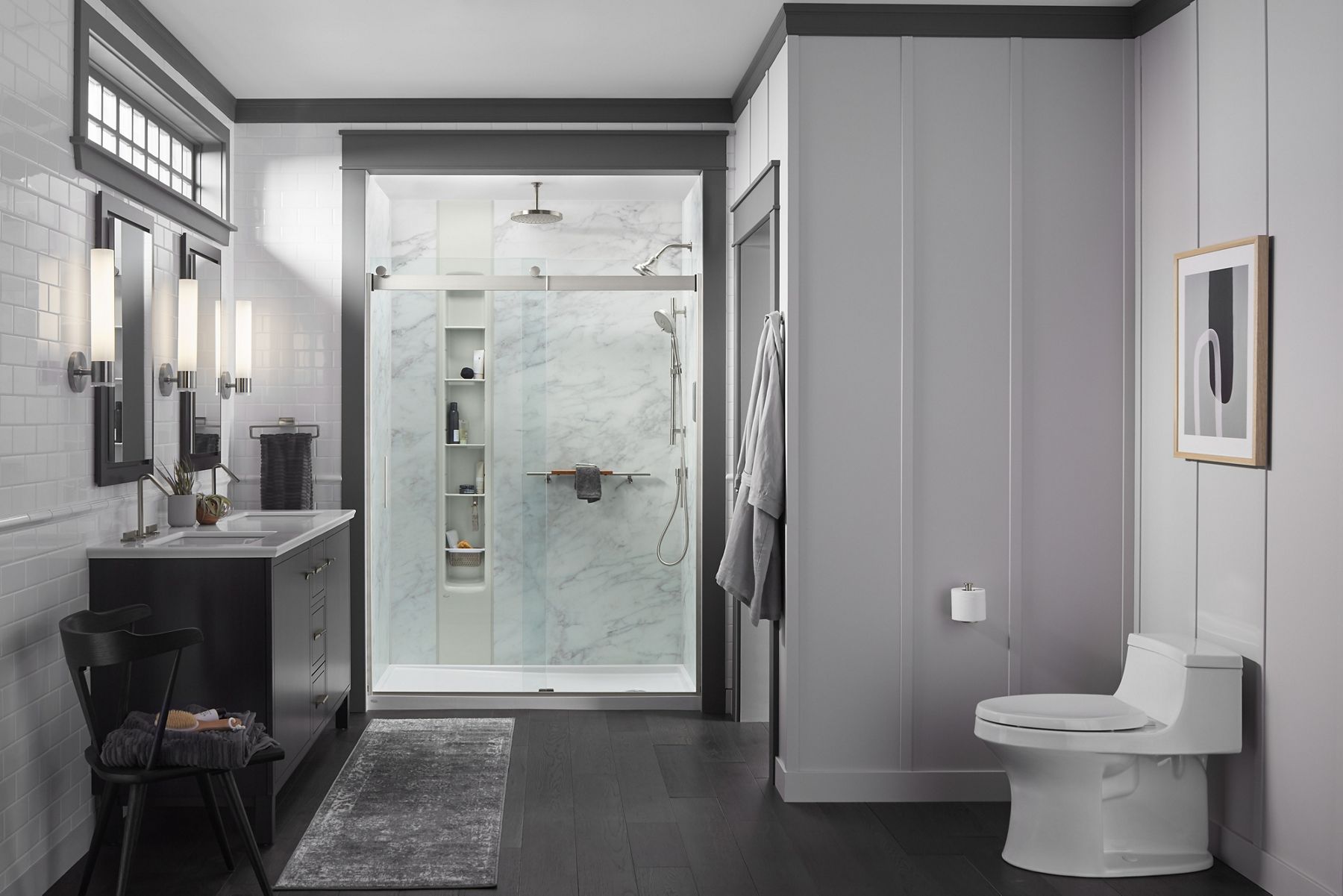 A bathroom in shades of gray with a double vanity on the left, toilet on the right, and a shower with glass doors in the background.