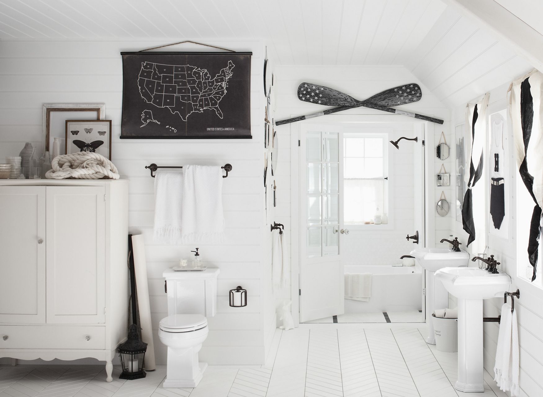 A white bathroom with modern and traditional elements, including a black wall map, crossed black and white oars, and black and white art and curtains.