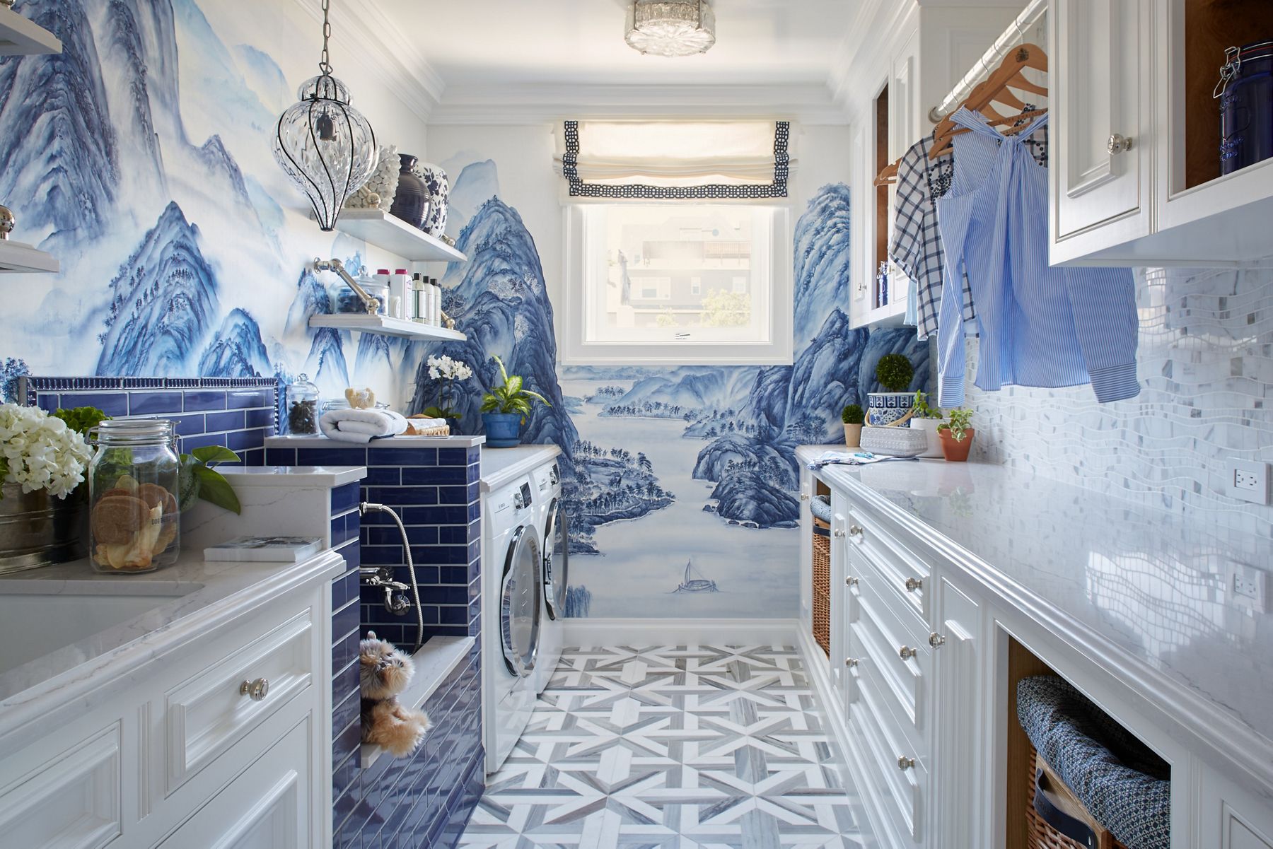 A utility room with bold patterned wallpaper, white tile floors, white upper and lower cabinets, and blue tiled pet washing station.