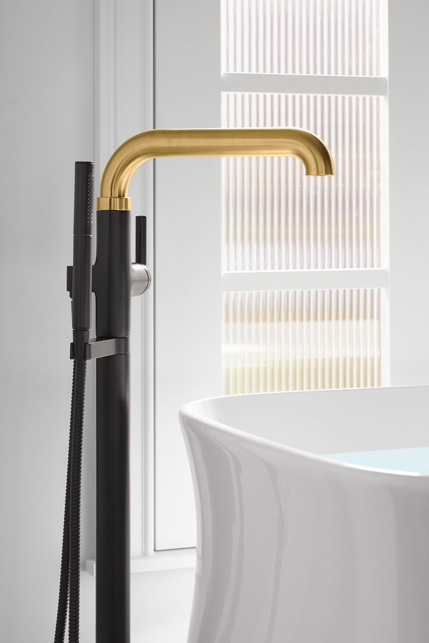 A two-tone brushed brass and matte black bath filler next to a white bath.