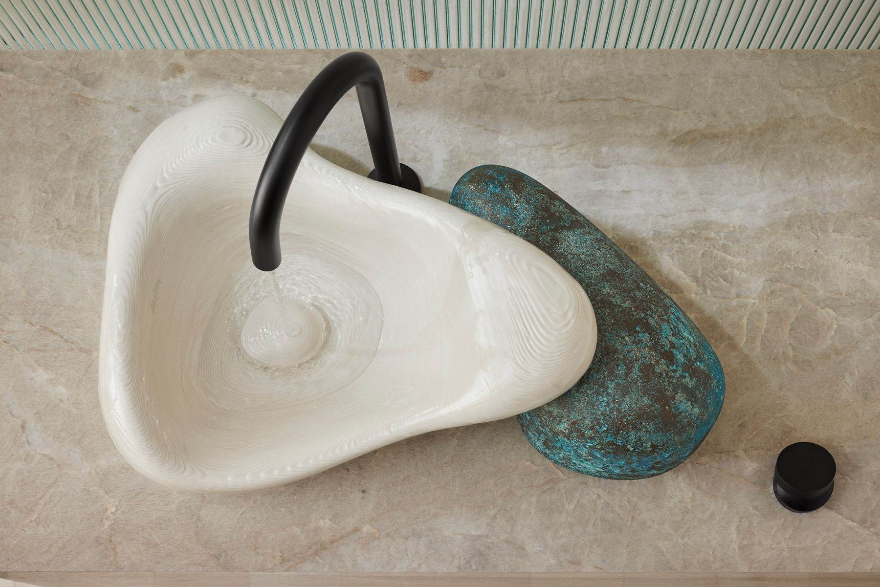 Close-up of a 3D-printed bathroom sink with a textured organic design, paired with a black faucet and a stone accent on a modern countertop