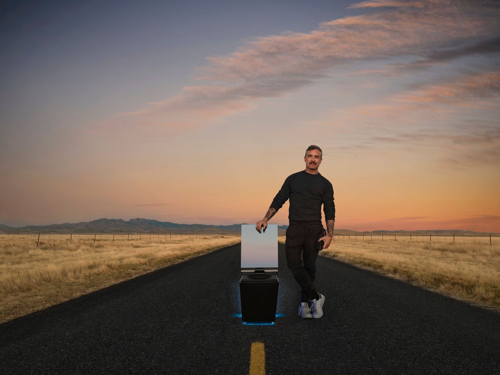 Portrait image of photographer and director Douglas Friedman posing next to the Numi 2.0 smart toilet in the middle of the road. It's sunset and the open lid of the toilet is reflecting brilliant colors. 