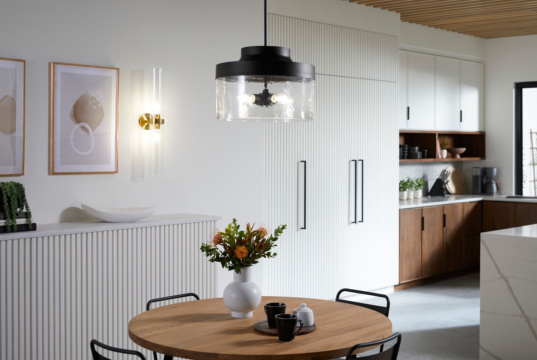 Une applique murale avec une base en laiton brossé et deux cylindres en verre clair orientés verticalement.