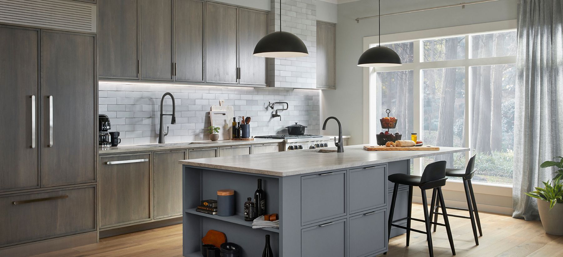 Contemporary kitchen with gray cabinetry, center island, pendant lighting, and a large window overlooking trees.