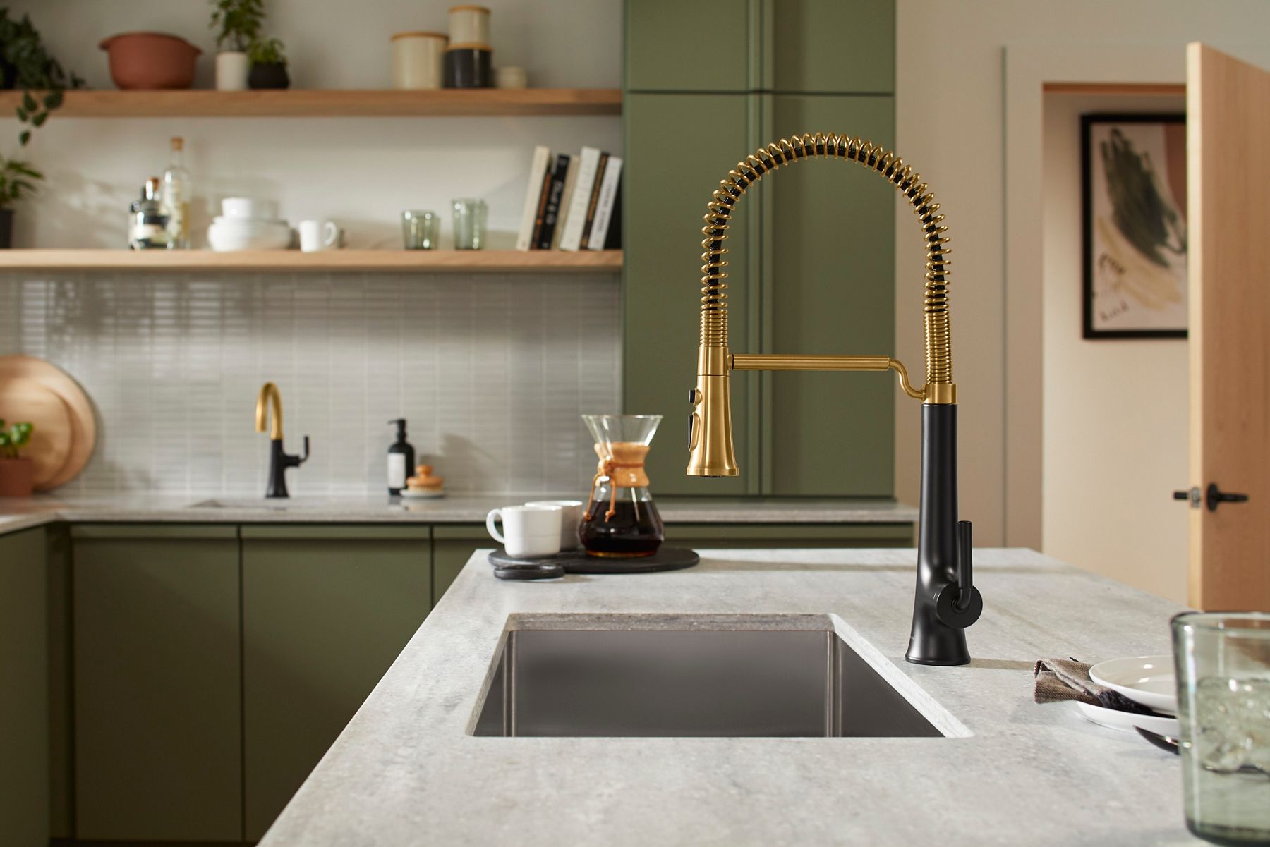 Kitchen sink with a two-tone pull-down faucet set against green cabinetry and open wood shelving.