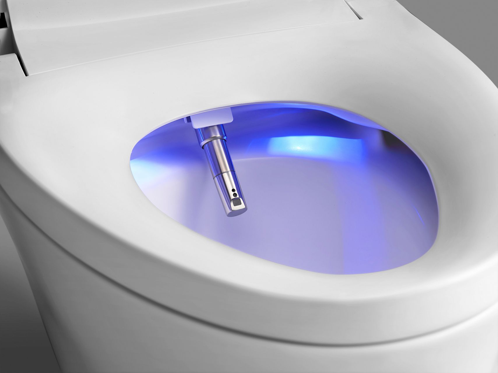 A toilet with a nightlight illuminating the inside of the bowl in a darkened room.