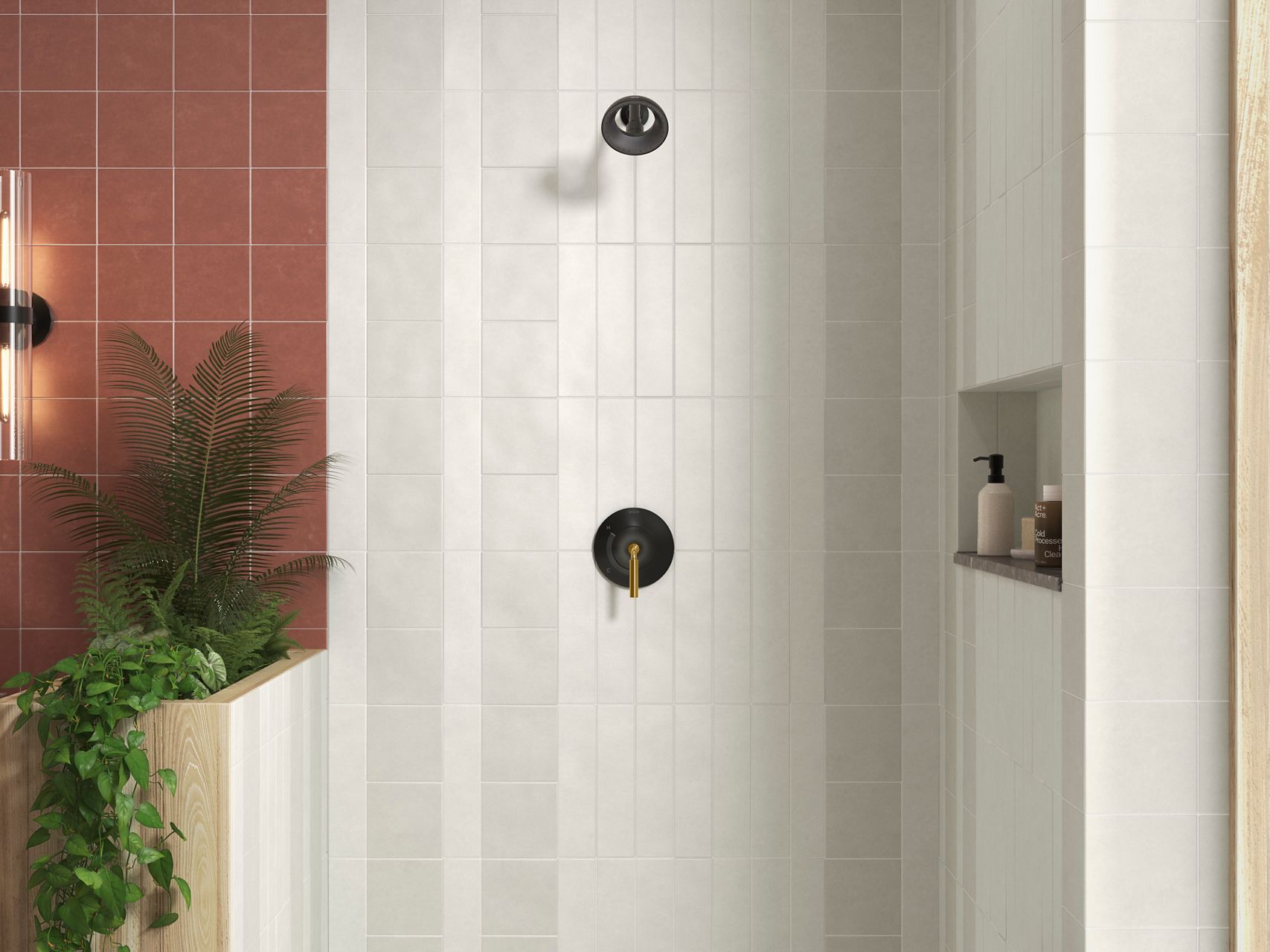 A shower with two-tone matte black and brushed brass handle, a matte black showerhead, and white tile.