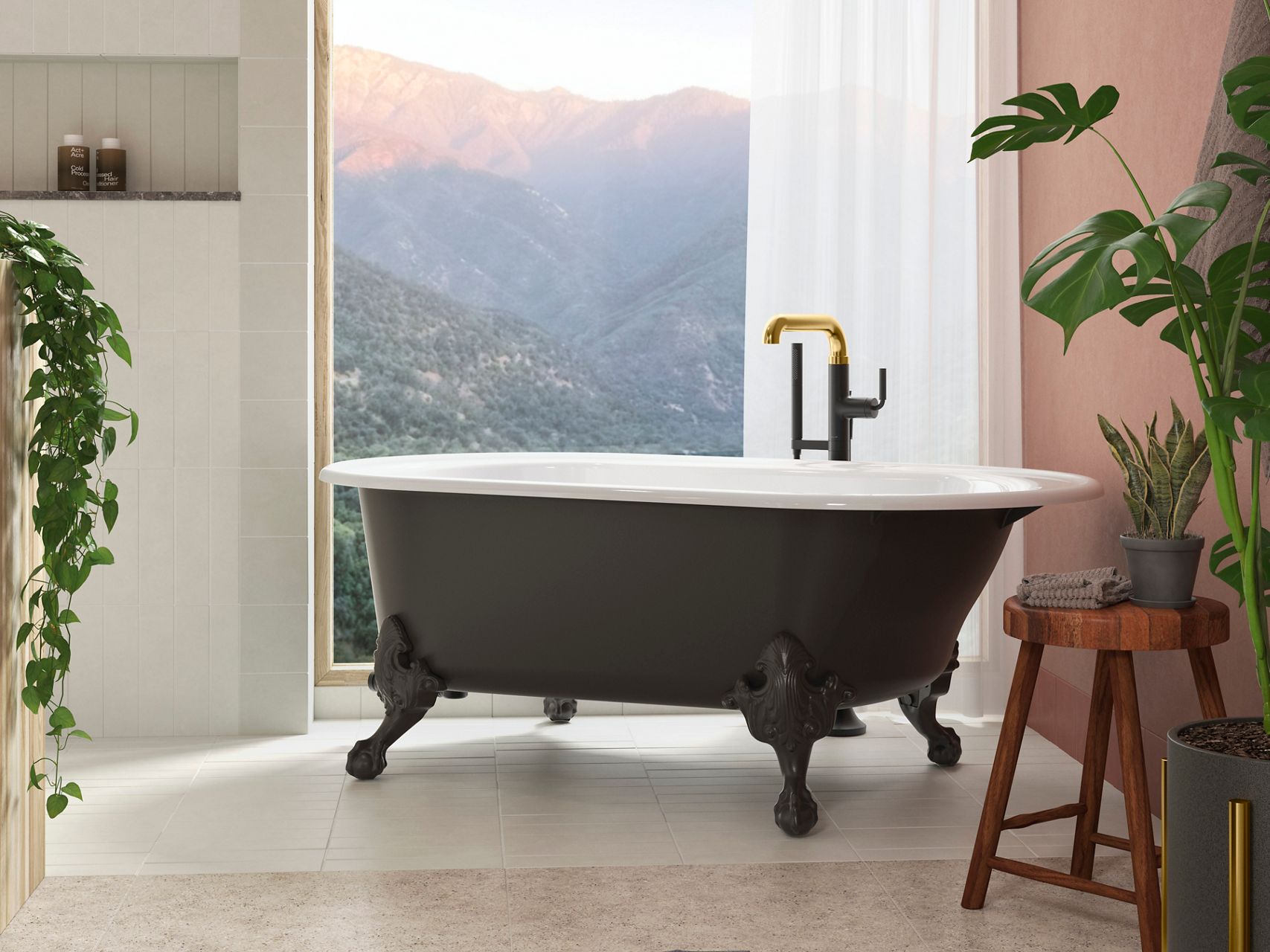 A freestanding bath with a black exterior and white interior, with a matte black and brushed brass bath filler in front of a window looking out to a mountain sunrise.