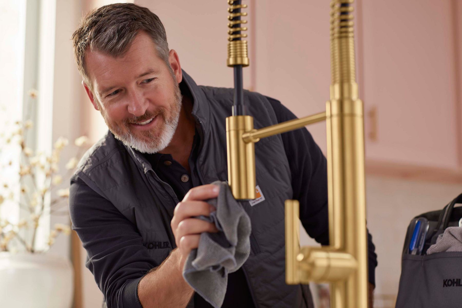 Smiling male professional polishing a gold kitchen faucet, representing trained and trusted installation experts.