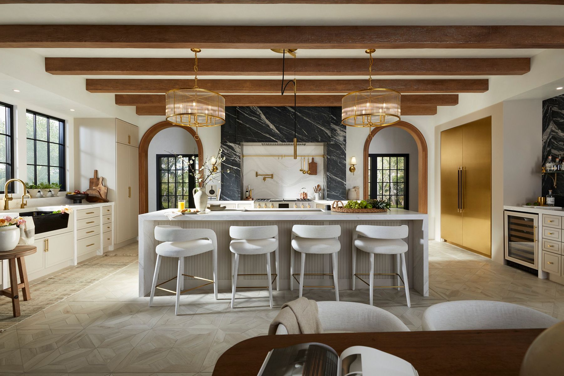  A kitchen in tones of cream, slate gray, brass. and white, with an island with seating.