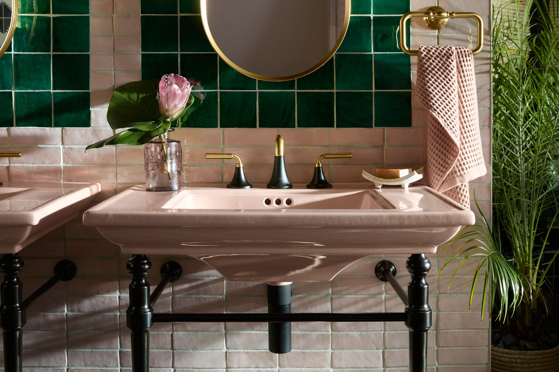 Image of the vanity sink area in bathroom designed by Justina Blakeney for Kohler's Heritage Color collection. Image focuses on the Peachblow console table sink with matte black and gold two-tone faucet and dark table legs.