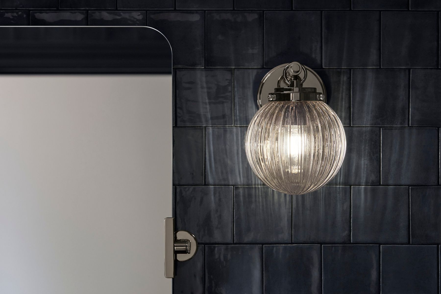 A chrome and glass sconce light on a dark blue tile wall.
