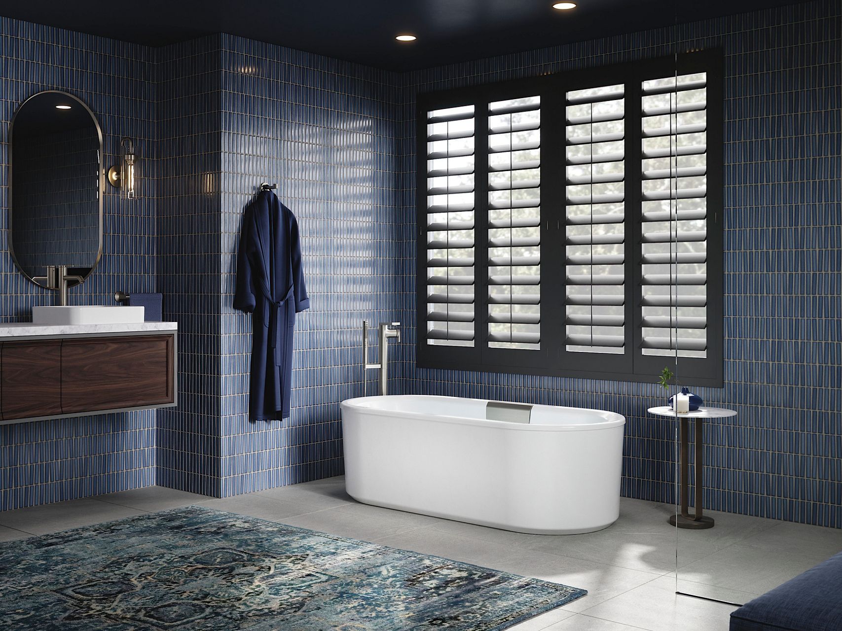 Modern bathroom with deep blue tiled walls, a white freestanding bathtub, dark wood vanity, and black-framed shuttered windows.