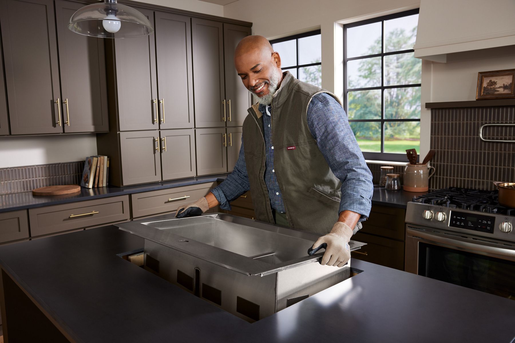 Professional installer, placing a stainless steel farmhouse sink in a modern kitchen setting.