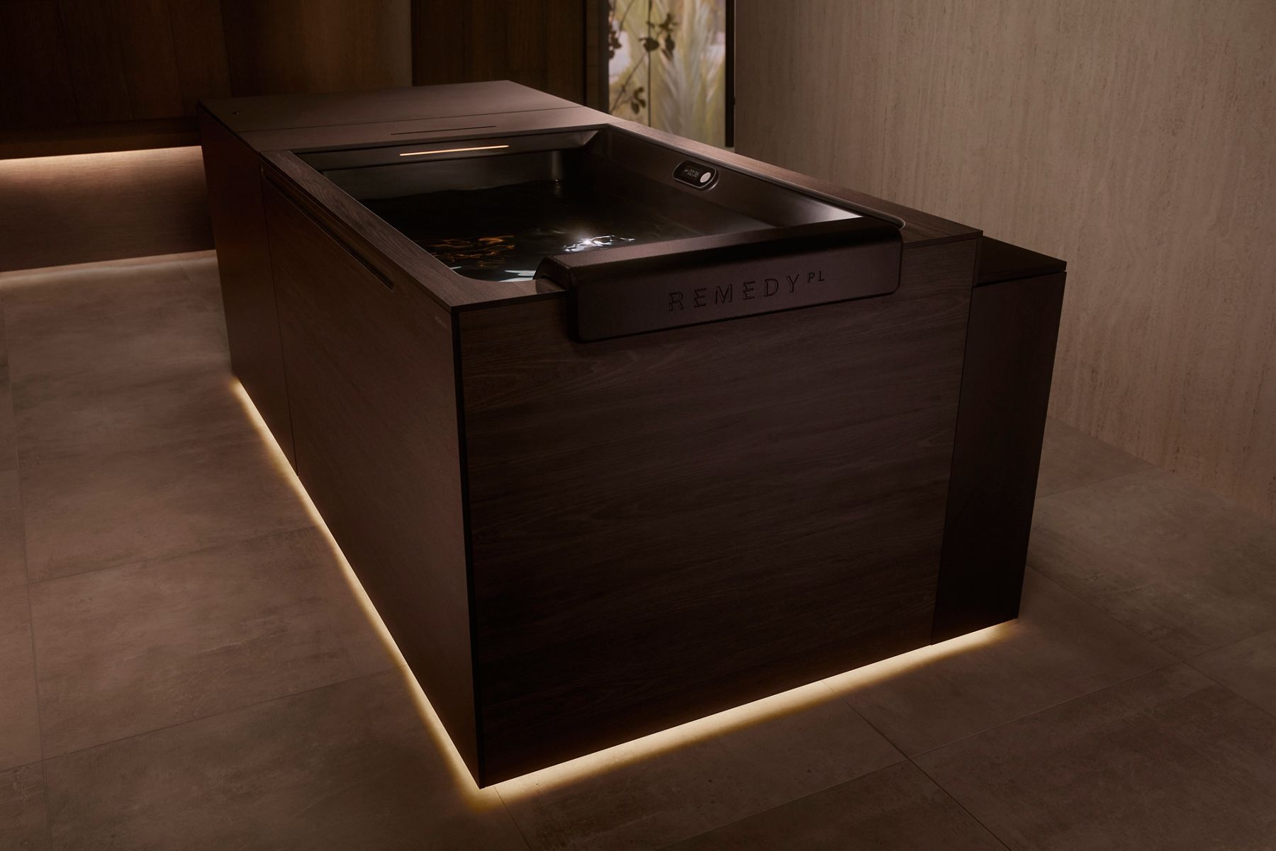 Vue rapprochée de la baignoire pour bain de glace Remedy Place, avec ses panneaux en bois foncé et son intérieur noir mat. La bordure de la baignoire comporte la marque « Remedy PL ». L’eau à l’intérieur de la baignoire est immobile et le panneau de commande intégré est visible, ce qui met en valeur le style moderne et luxueux de la baignoire dans une salle de bain chaleureuse et légèrement éclairée.