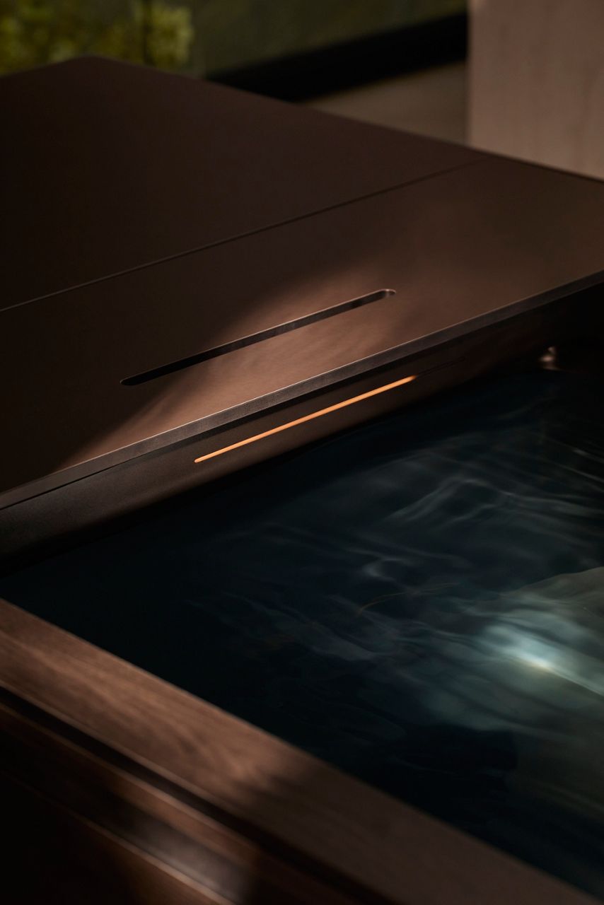 Gros plan sur le bord de la baignoire pour bain de glace, qui présente une surface élégante noir mat, avec une fine bande lumineuse intégrée qui émet une lueur chaleureuse. La douce ondulation de l’eau ajoute un sentiment de calme et de luxe à l’ensemble de la conception, soulignant l’esthétique moderne et raffinée de la baignoire.