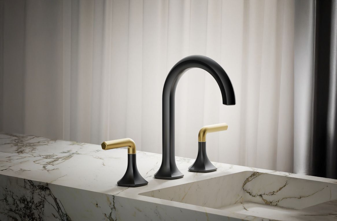 Matte black bathroom sink faucet spout and two-town matte black and brushed brass lever handles mounted on a marble countertop.