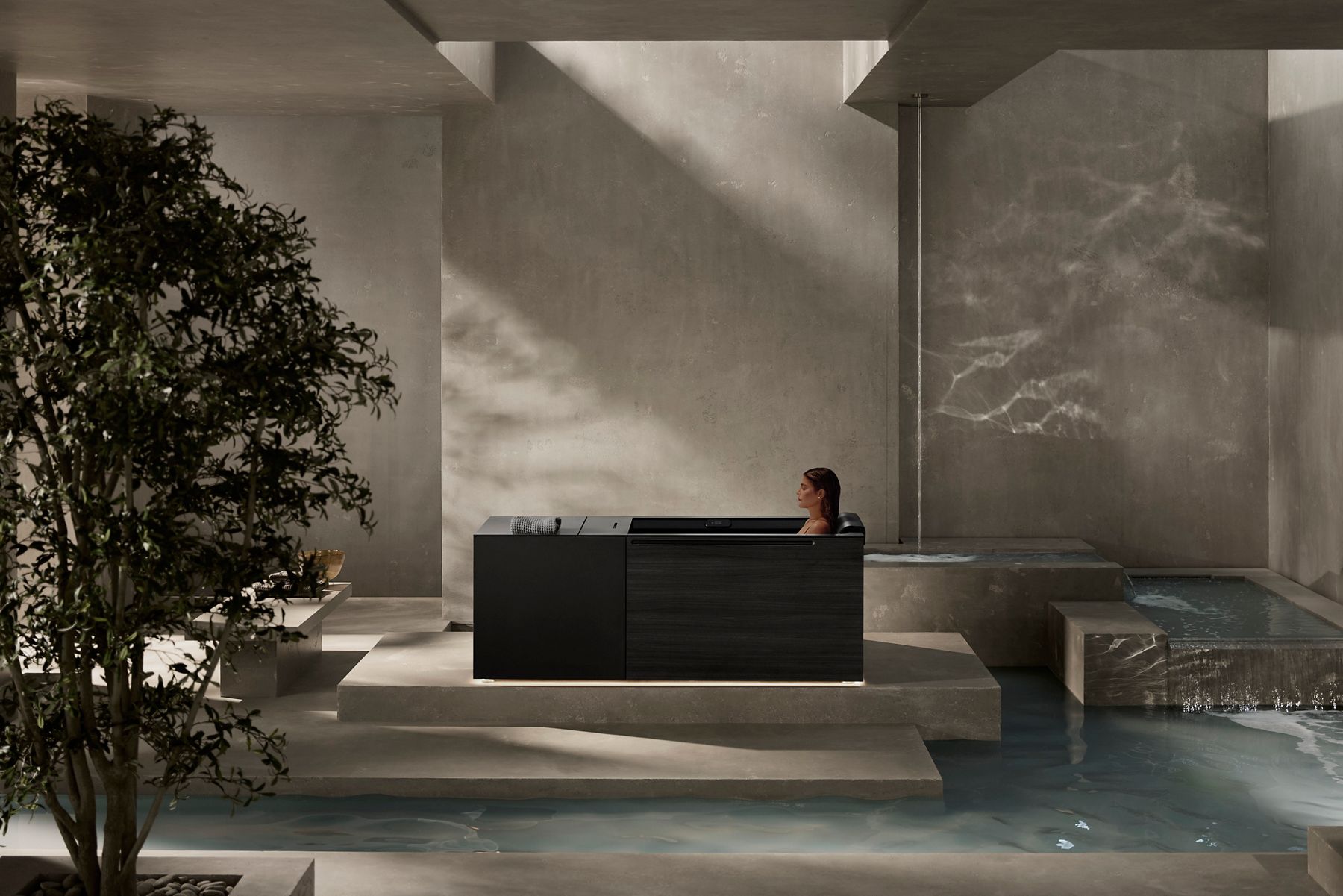 Woman soaking in a KOHLER Ice Bath within a serene spa environment, featuring light stone and glistening pools of water.