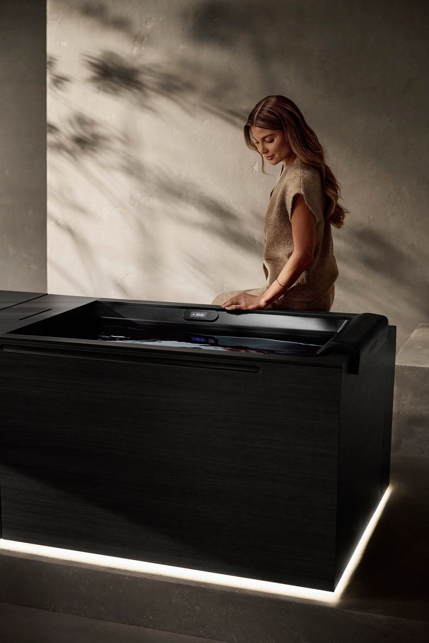 A woman sitting on the edge of a Kohler Ice Bath looking into the water.