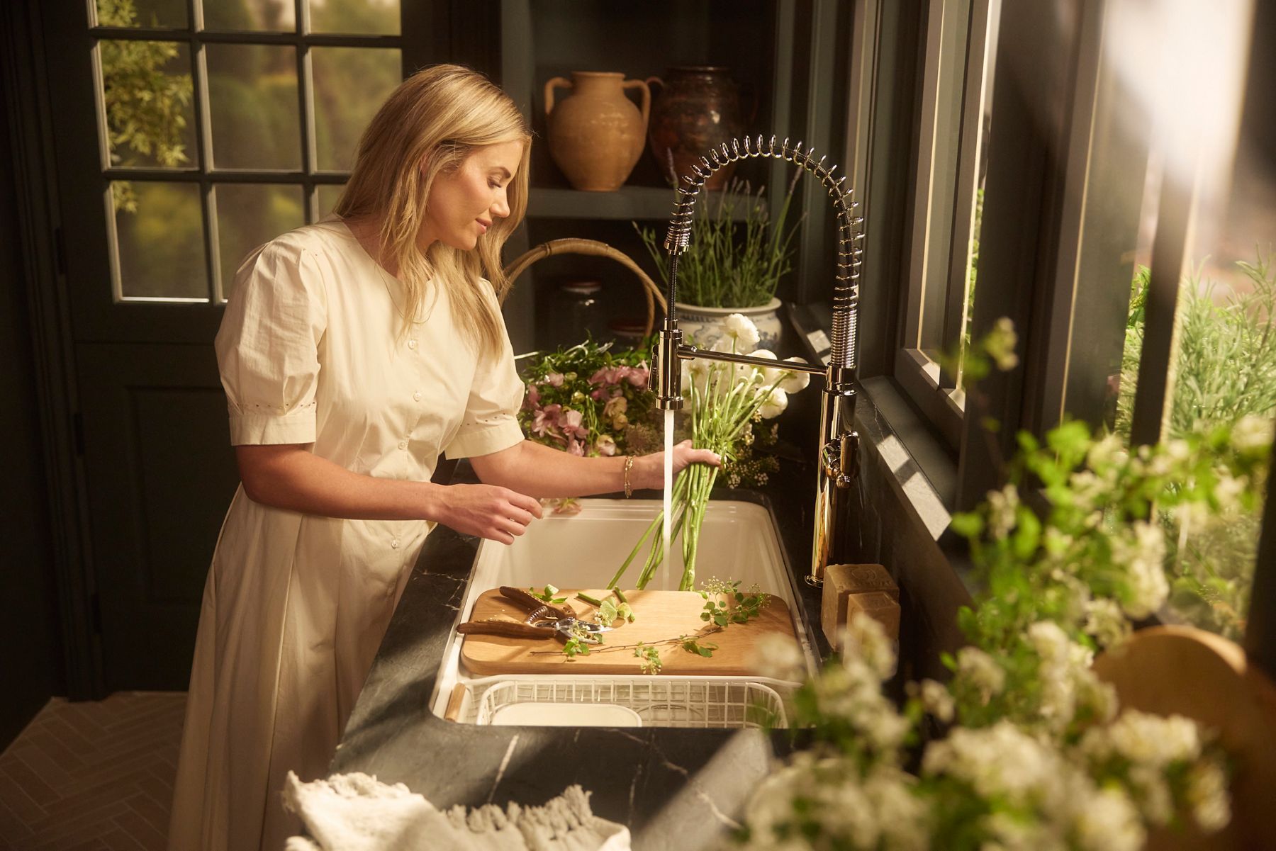 Shea McGee rinses fresh herbs at the Audrine™ farmhouse workstation sink using integrated accessories and a high-arc faucet.