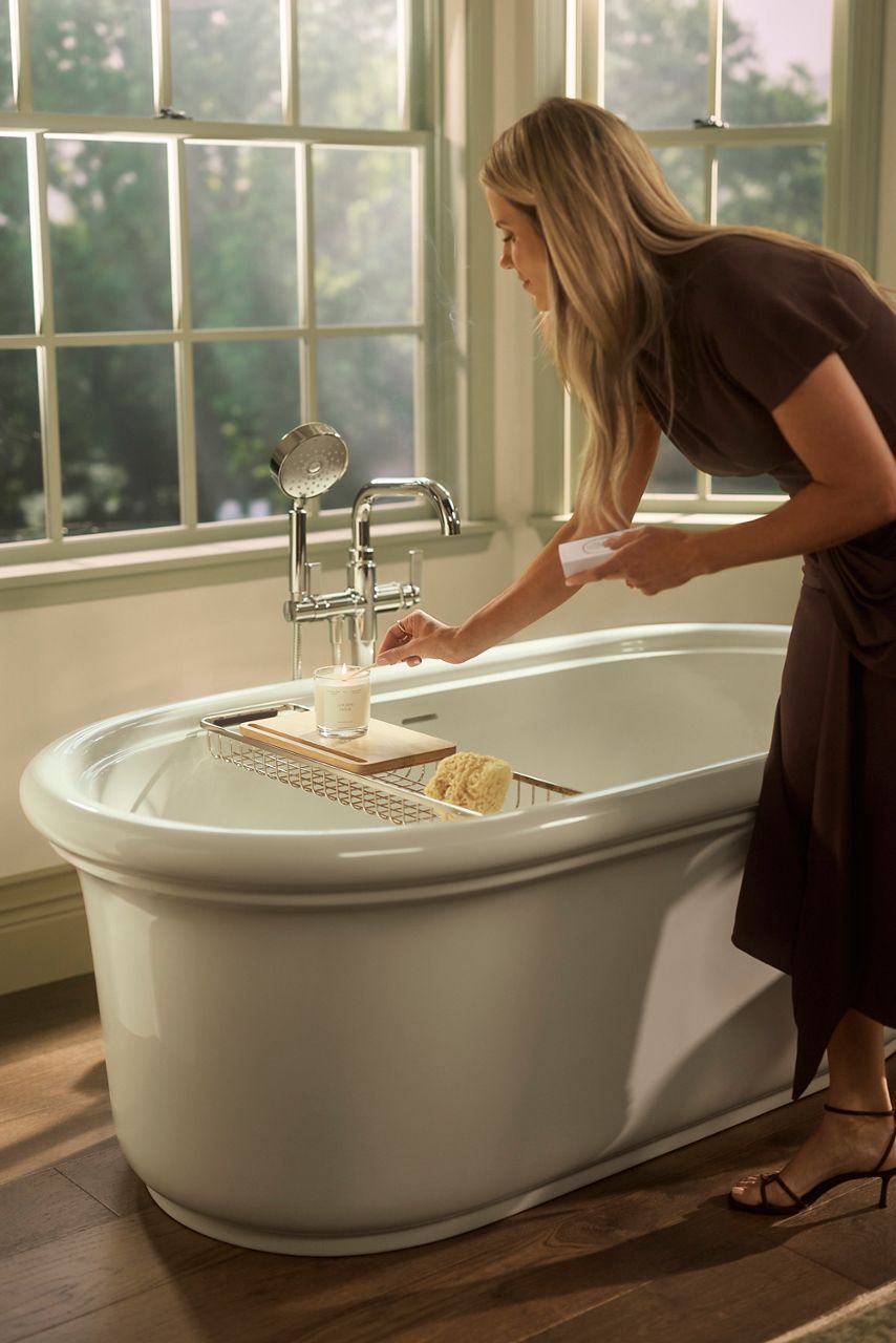 The Claude freestanding bath and the Castia floor-mount bath filler in silver sit next to an open window with afternoon light pouring in.