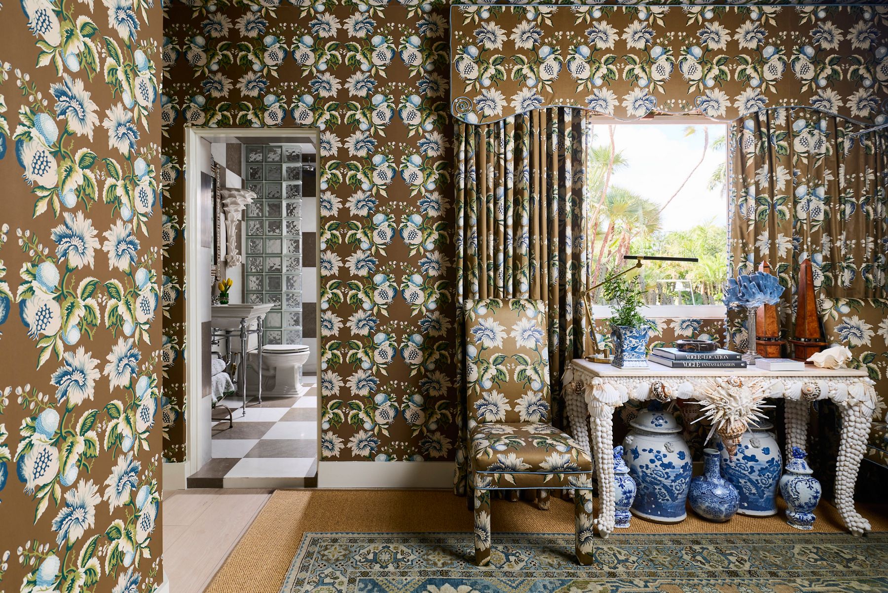 Elaborate wallpapered bedroom with matching textiles peeking into vintage-inspired bathroom.