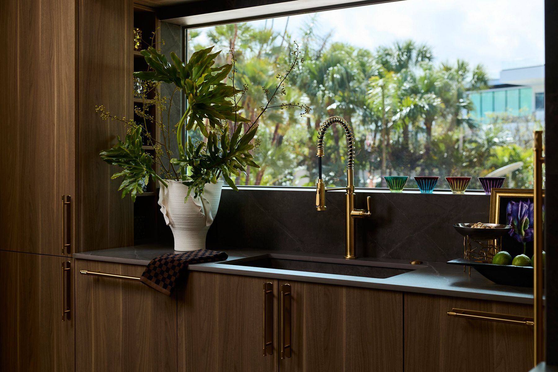 Sophisticated kitchen sink and gold-toned faucet with a view of palm trees.