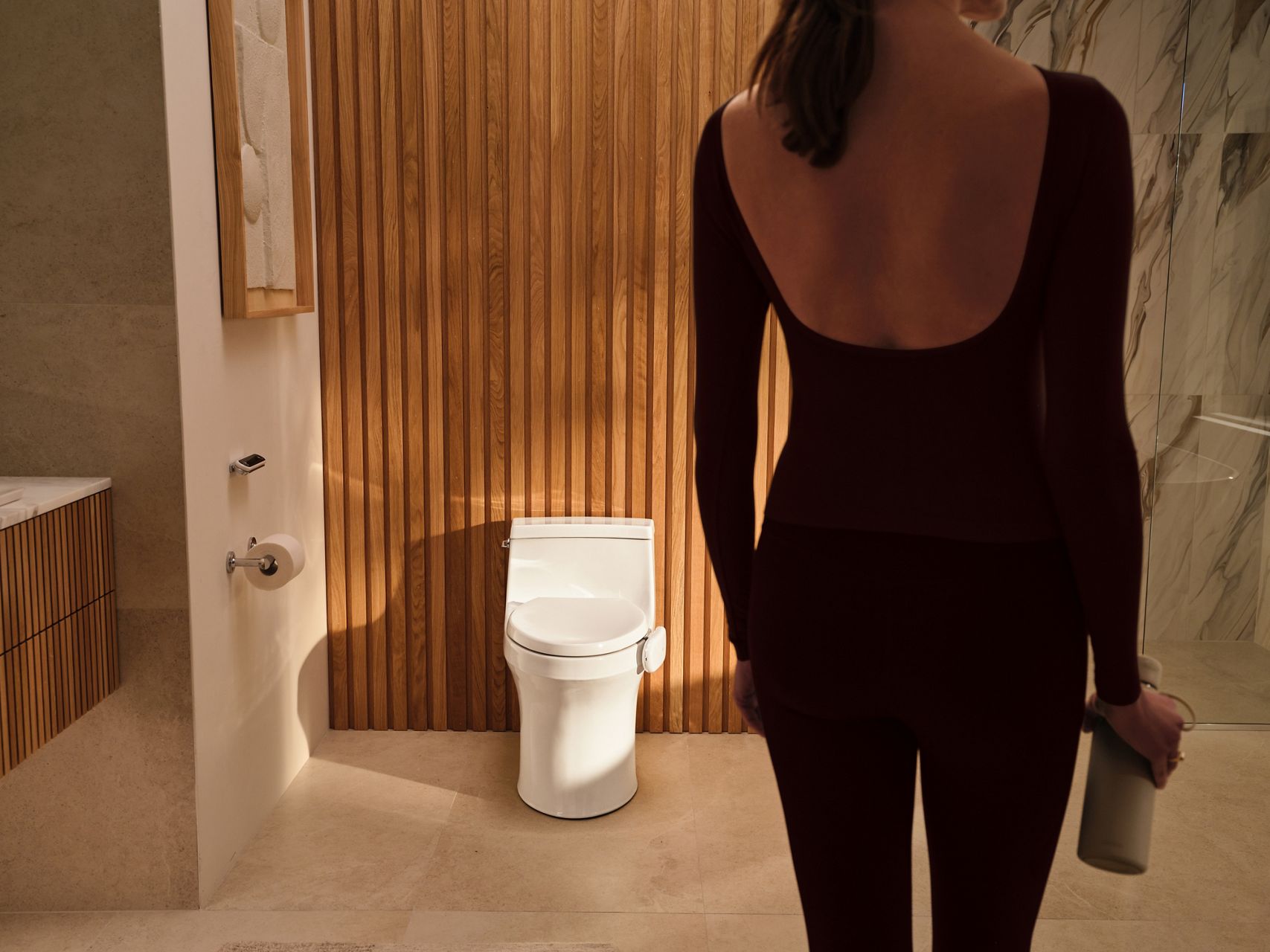 Modern bathroom featuring a toilet equipped with the Kohler Health Dekoda device as a person walks toward it.