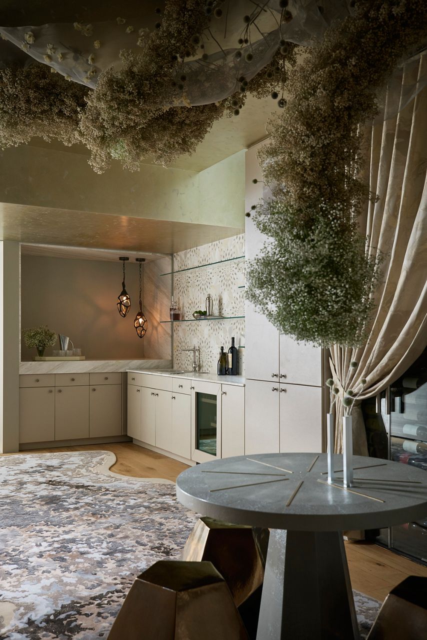 Contemporary kitchen and dining space with cream cabinetry, stone countertops, sculptural floral installations, and a round dining table.