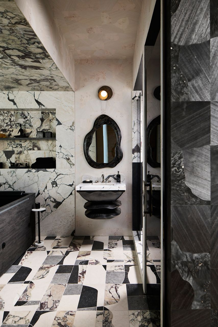Luxury bathroom featuring bold black-and-white veined stone, a sculptural floating sink, organic-shaped mirror, and geometric stone tile flooring.