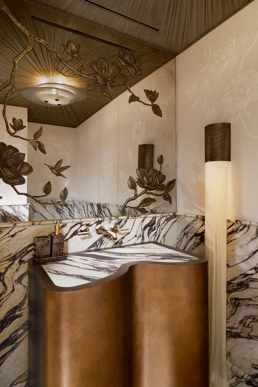 Elegant powder room featuring a sculptural bronze vanity with dramatic veined stone countertop, floral wall reliefs, brass fixtures, and decorative botanical ceiling details.
