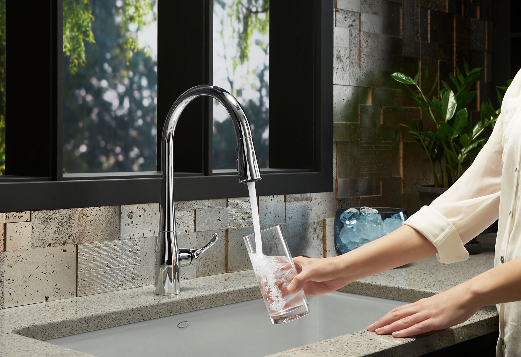 A hand holding a glass under a kitchen faucet with water filling it.