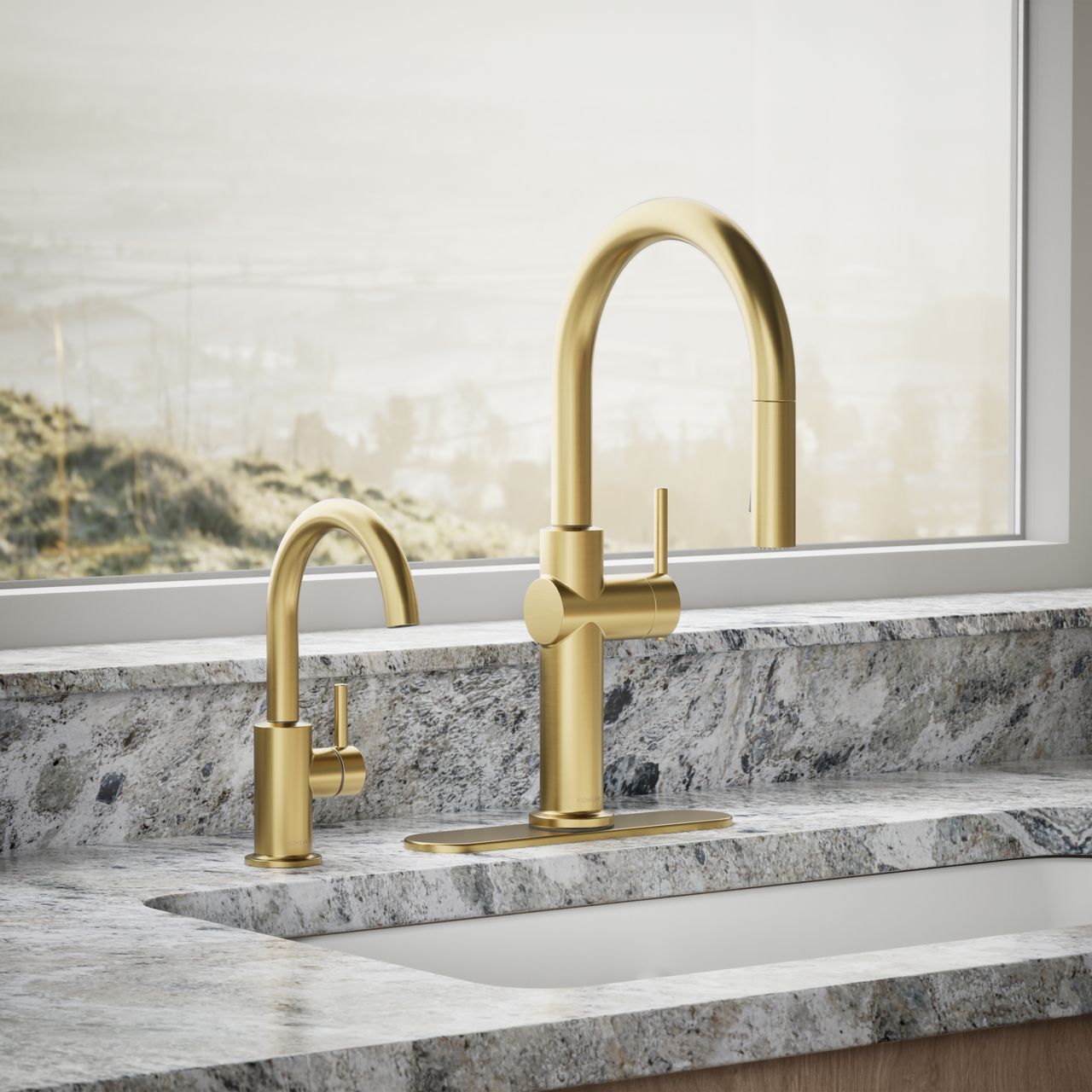Close-up of gold kitchen faucet and matching bar faucet set against a stone countertop and window view.
