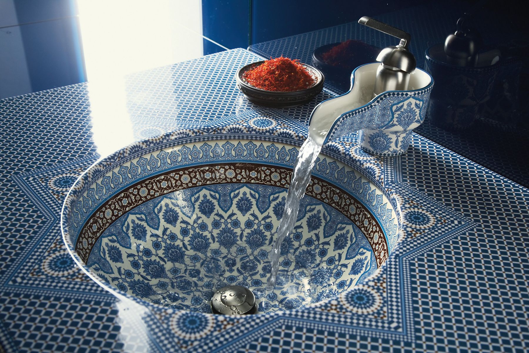 Blue patterned ceramic vessel sink with ornate design and running water faucet.