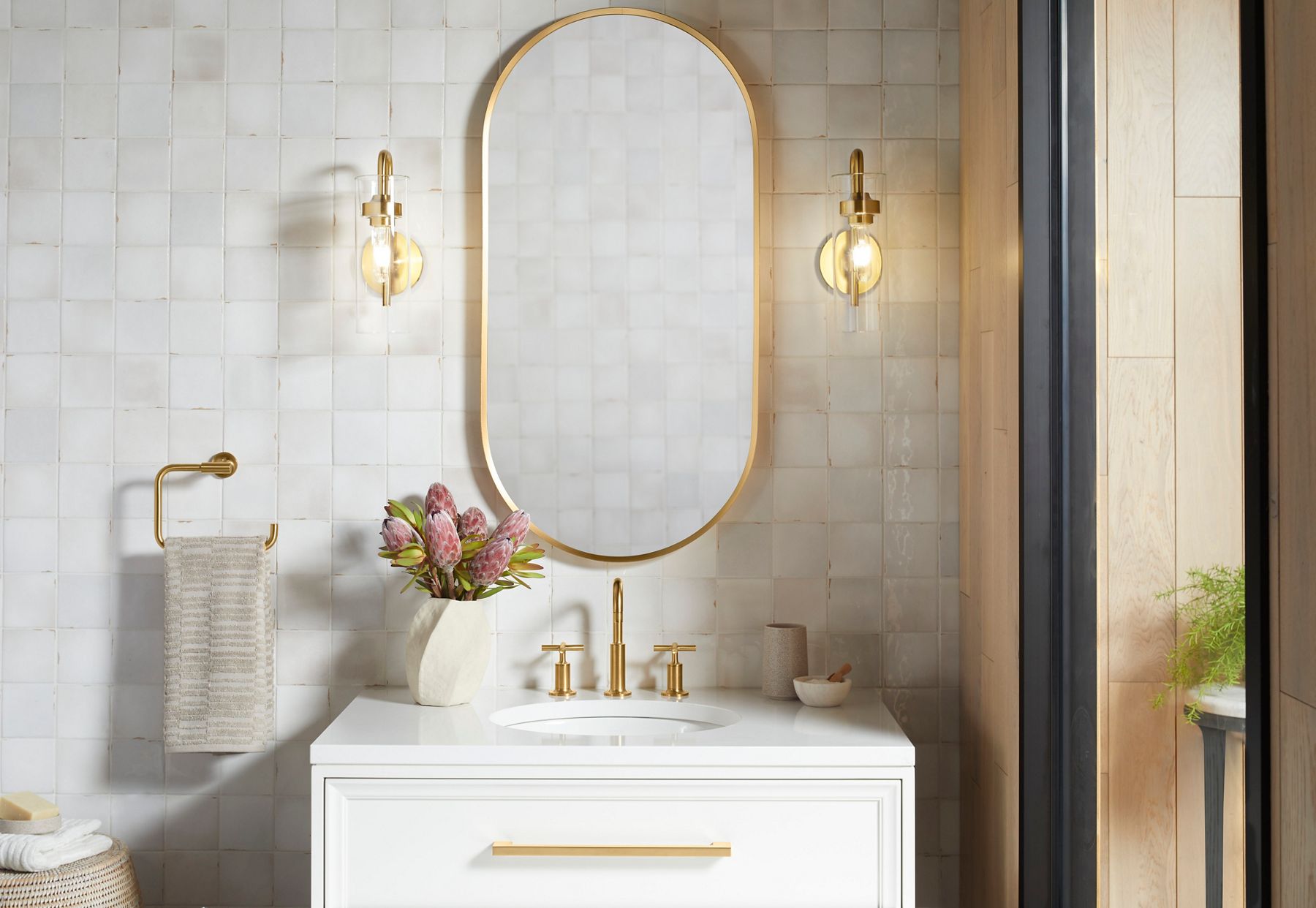 Bathroom vanity setup with brushed gold faucet, oval mirror, and gold accents