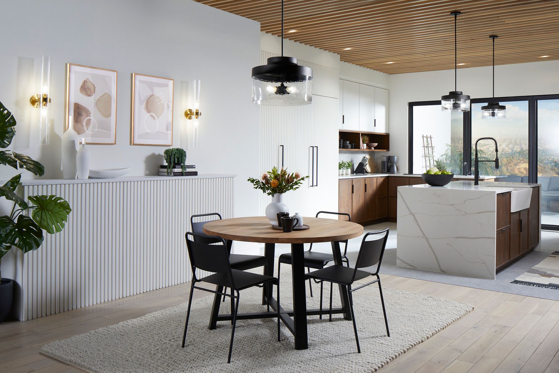 An open concept home, with round dining table, and white marble waterfall island with KOHLER Purist kitchen sink faucet in Matte Black, and Purist pendant lights.