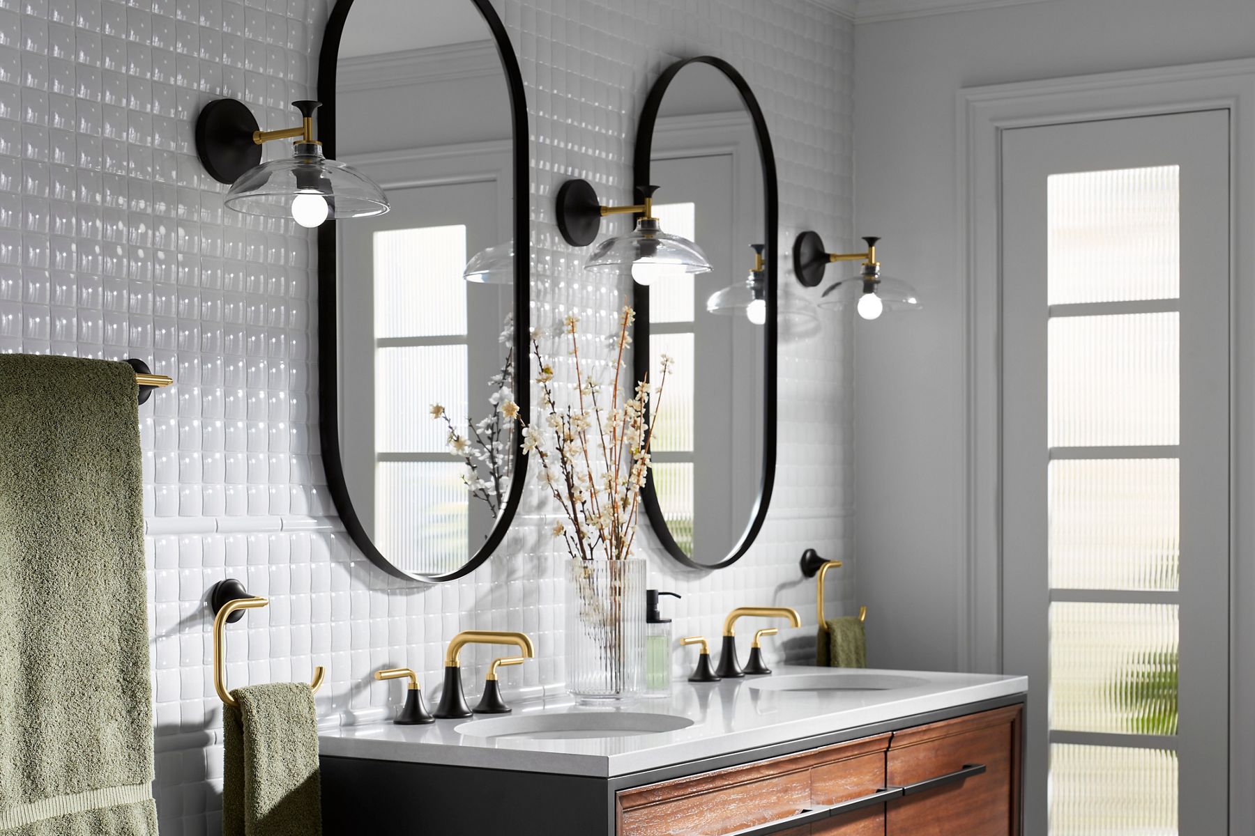 Contemporary bathroom with dual oval mirrors, white tile backsplash, brass faucets, and glass wall sconces.
