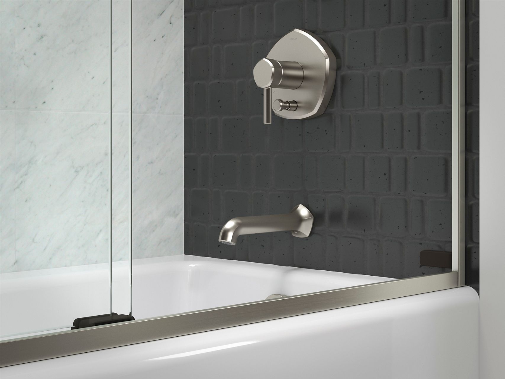 A bathtub area with a brushed nickel faucet and sliding glass door, and with one wall of a large light gray stone tile and another of small dark gray tiles.