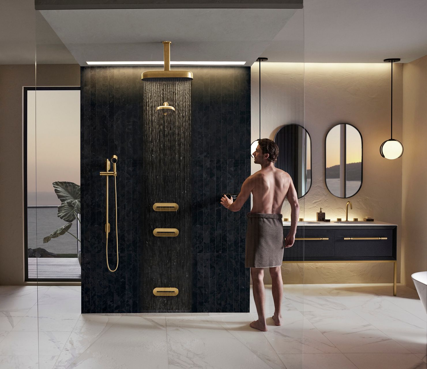 A man in a towel turning on the water to an open shower area with multiple outlets in brushed brass.