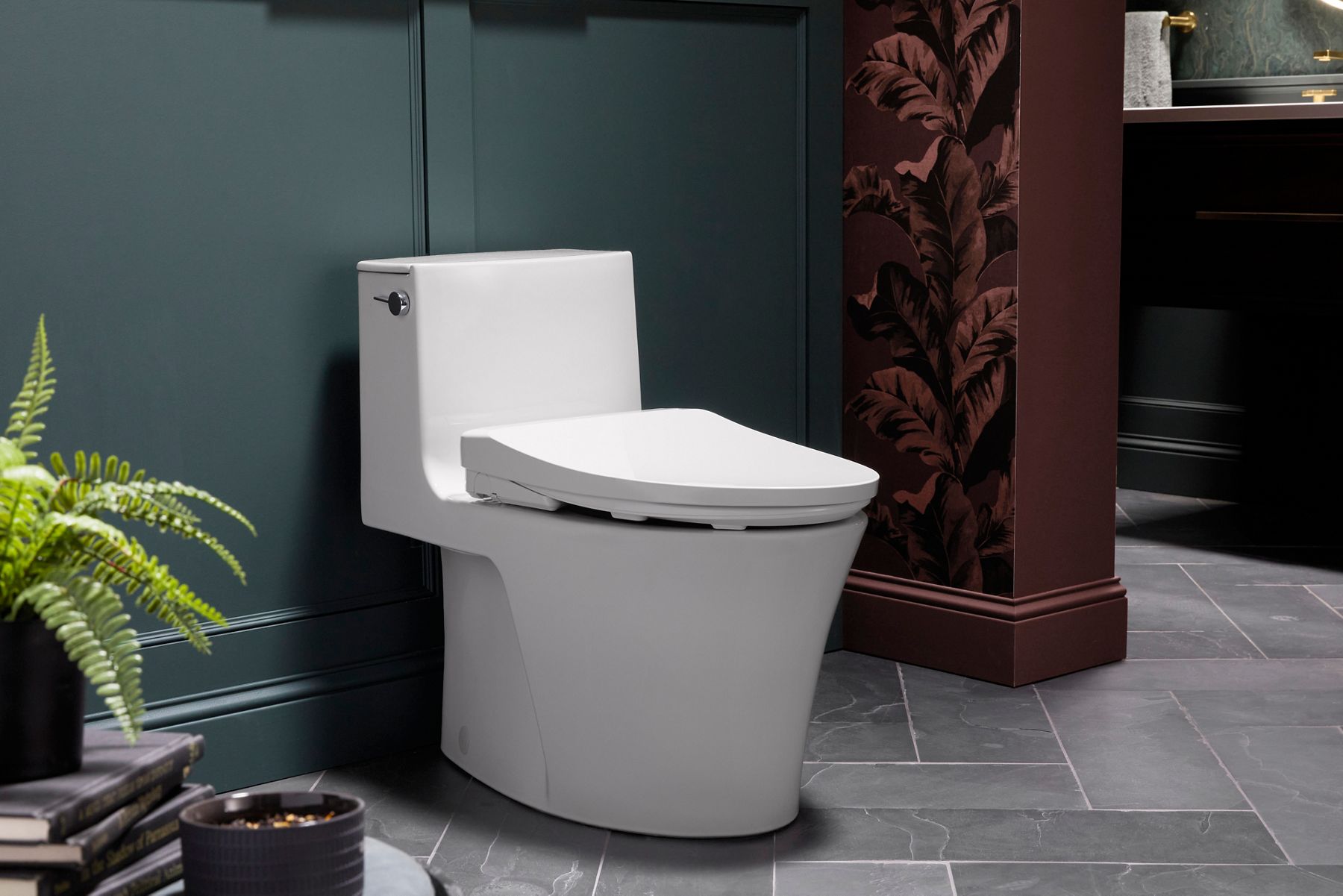 Modern white smart toilet in dark green bathroom with fern plant and slate flooring.