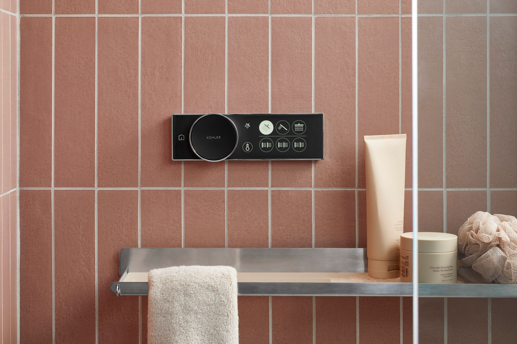 KOHLER smart shower control panel mounted on a light brown tiled wall, featuring a circular dial and illuminated touch buttons for various water settings.