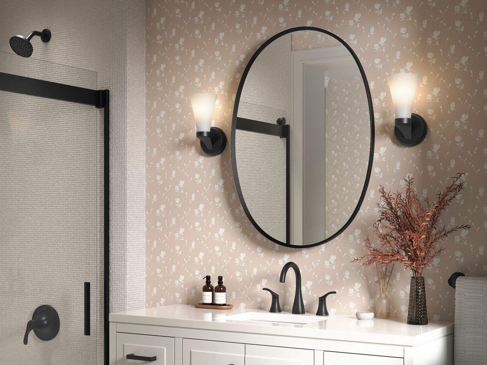 Large oval black-framed mirror with matching black sconces over a white vanity and patterned wallpaper.