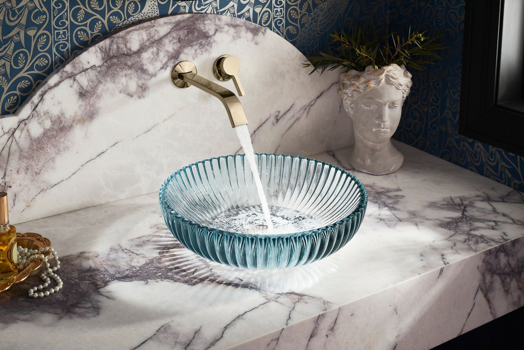 Decorative wall-mounted faucet with running water into a ribbed light blue glass sink.