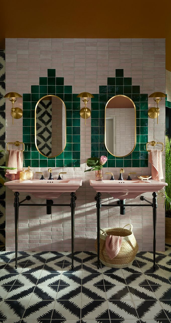 Two narrow oval mirrors framed by green geometric tile and brass sconces in an art deco–inspired bathroom.