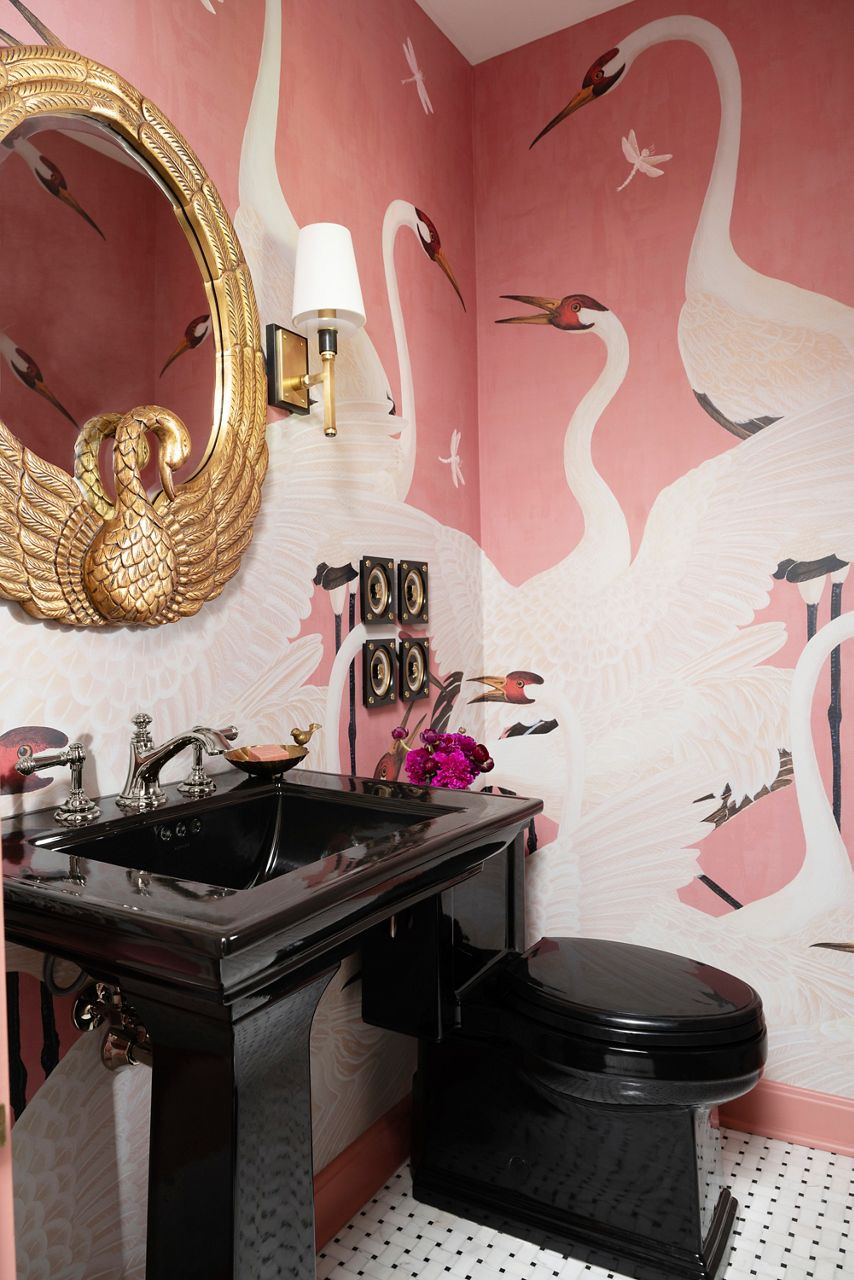 A stylish powder room featuring a black sink and fixtures complemented by mixed metals and a pink wallpaper with a swan motif.