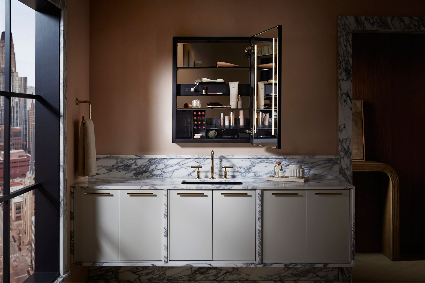 Wall-mounted medicine cabinet mirror with integrated shelves above a marble countertop and brass fixtures.