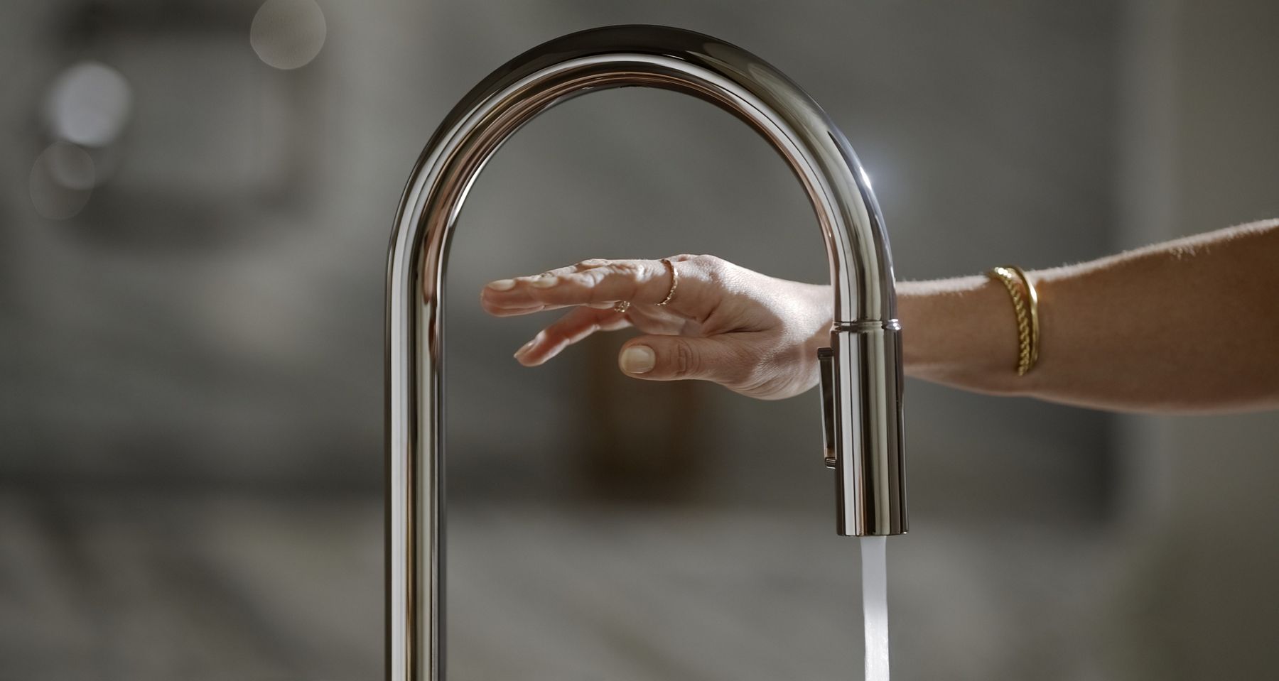 Hand reaching under a modern, touchless stainless steel kitchen faucet
