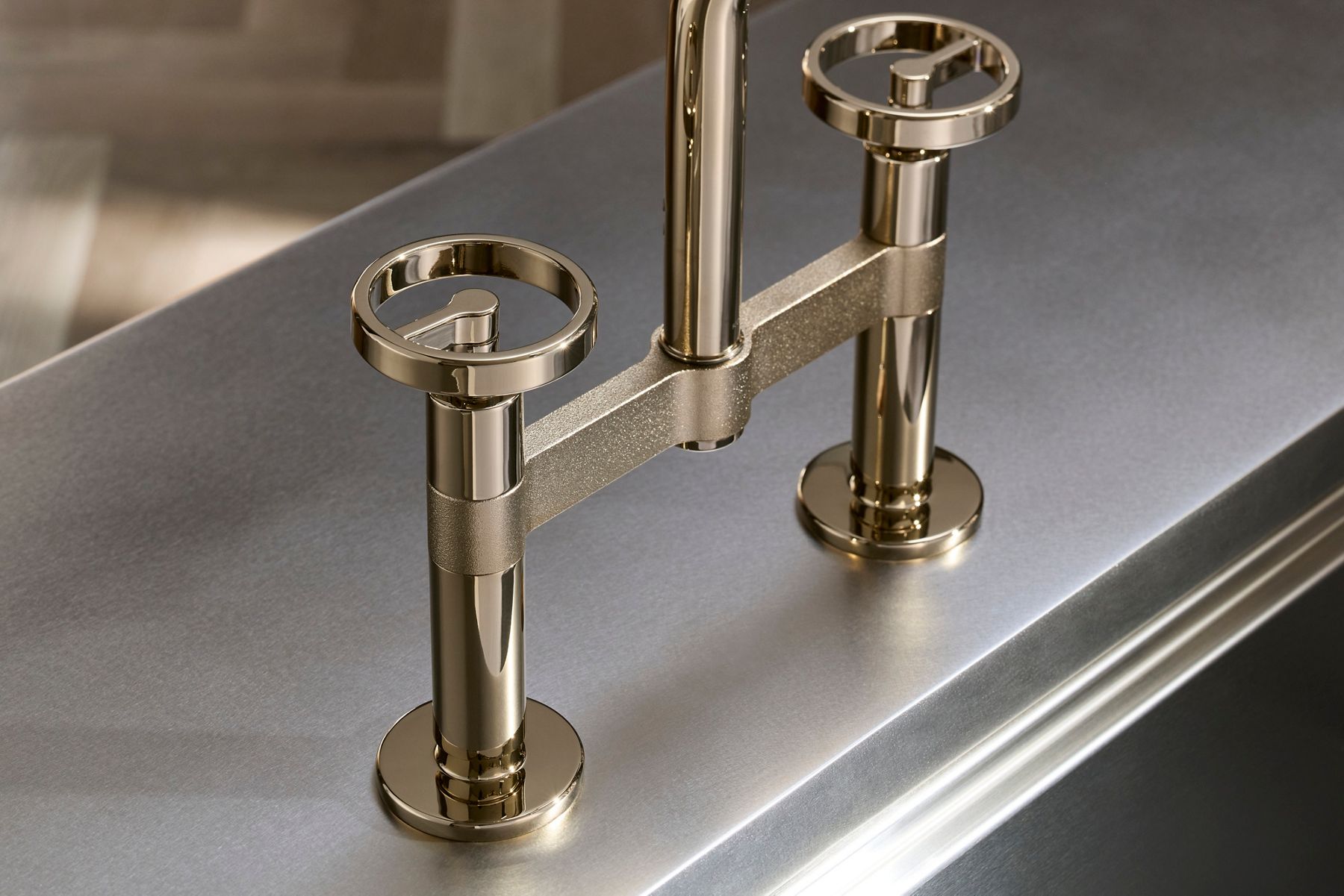 Close-up of a brass kitchen faucet with two valve-style handles on a stainless steel sink